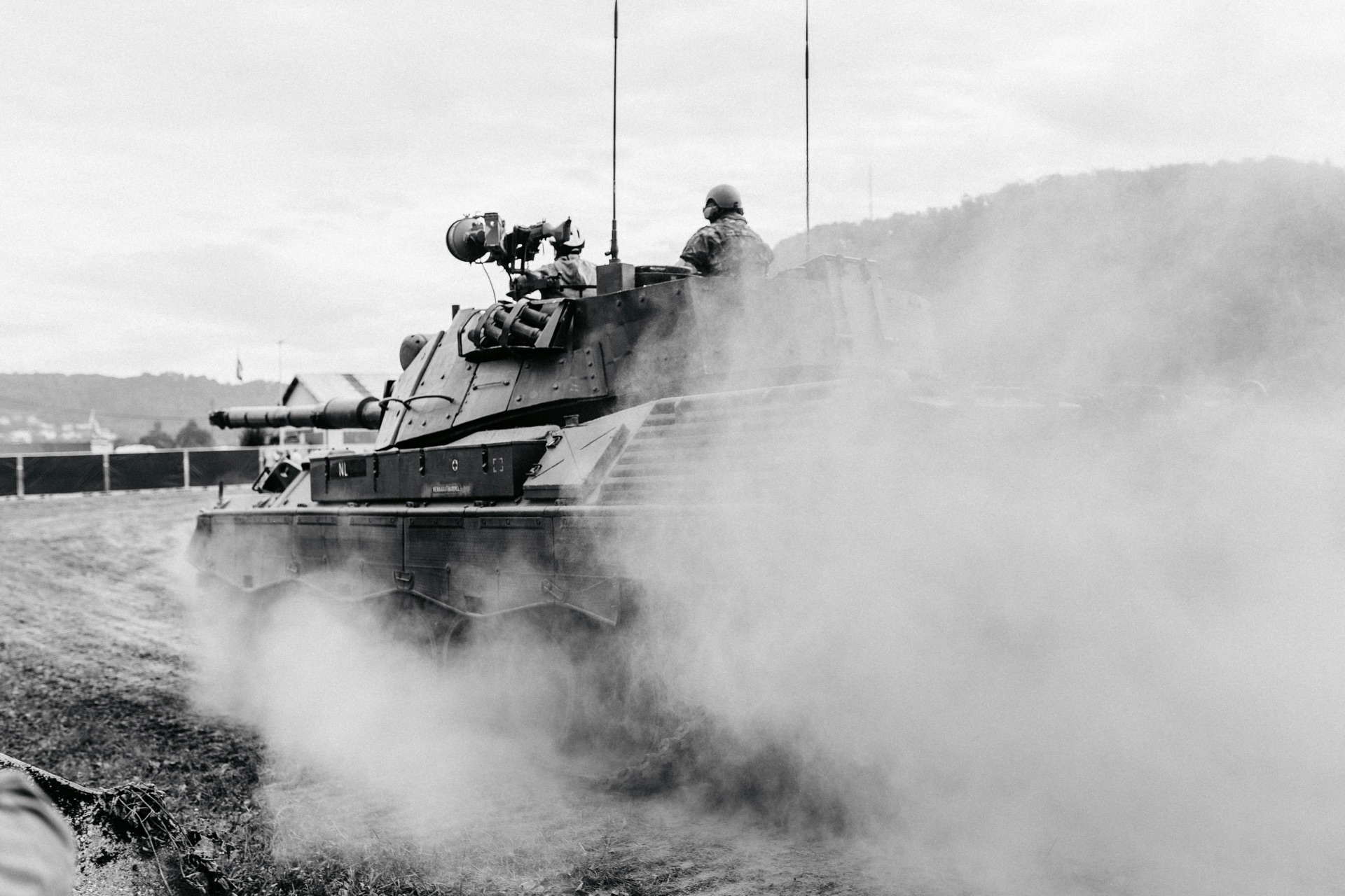 An armored vehicle crossing unsealed ground, throwing up a heavy cloud of dust.