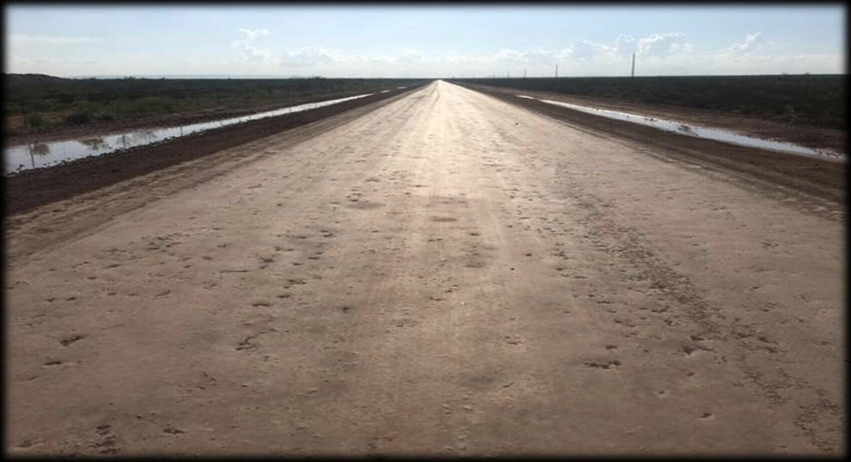 A stabilized haul road running to the horizon with standing water on both shoulders.