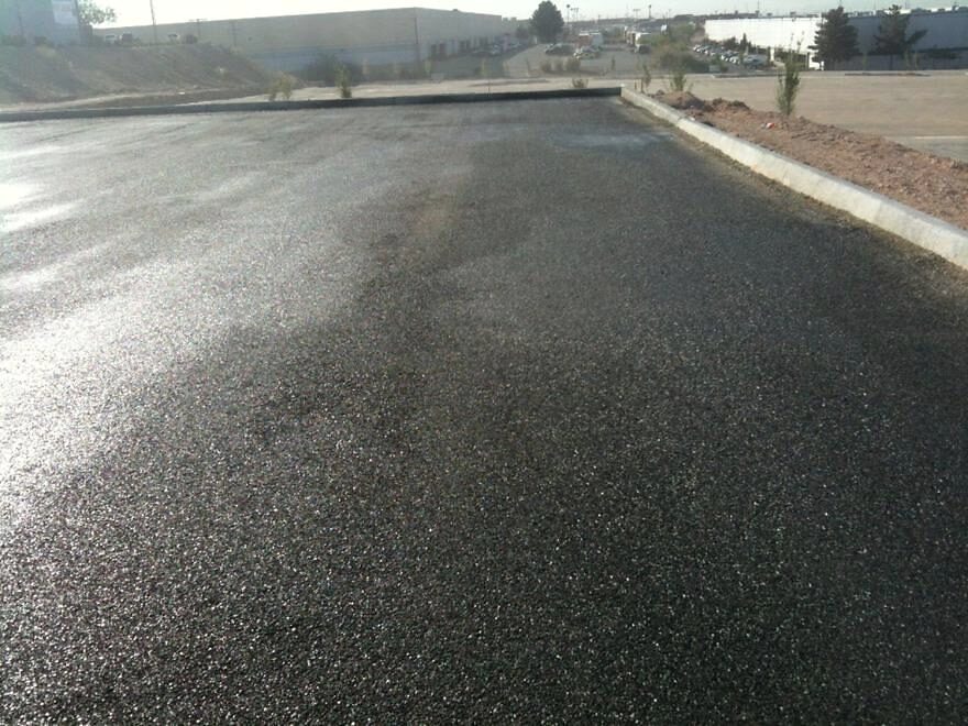 A freshly sealed asphalt surface, wet and dark, with a curb along one side.