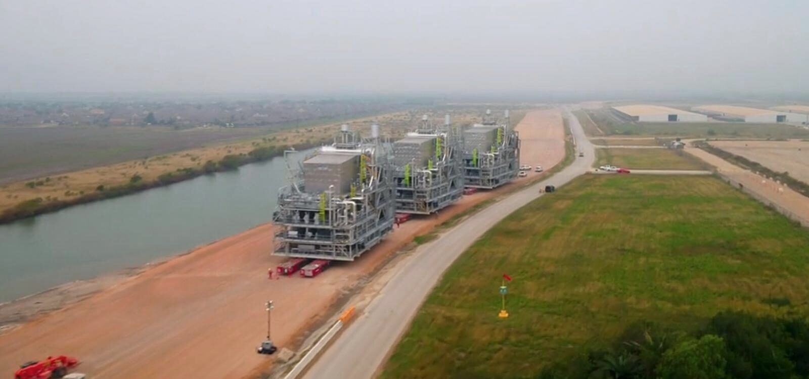 Process modules on transporters crossing a stabilized corridor beside a waterway.
